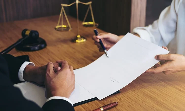 Contract handed across a desk with scales and a gavel