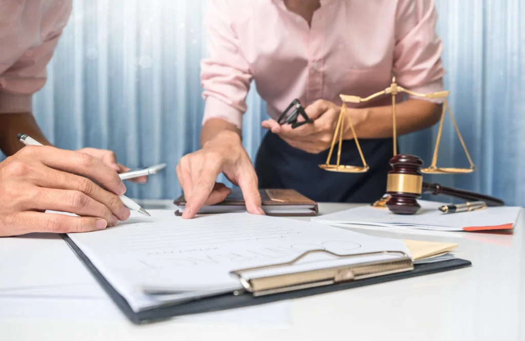 Two people reviewing a document on a clipboard beside scales and a gavel
