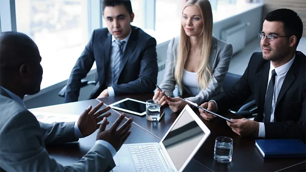 Four business people in a meeting around a table with a laptop and tablet