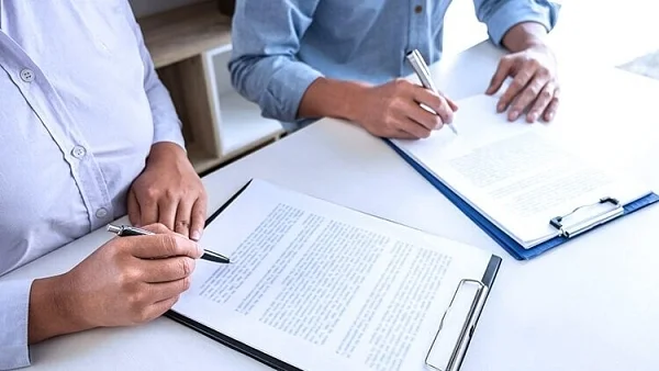 Two people signing documents on clipboards at a white desk