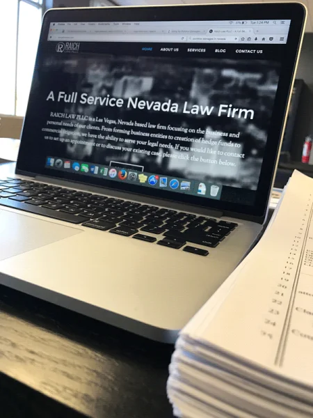 Laptop showing the Raich Law PLLC website, A Full Service Nevada Law Firm, beside a stack of papers