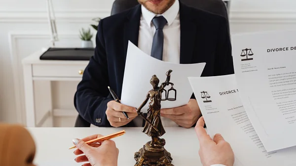 Man in a suit holding divorce papers at a desk behind a Lady Justice statuette