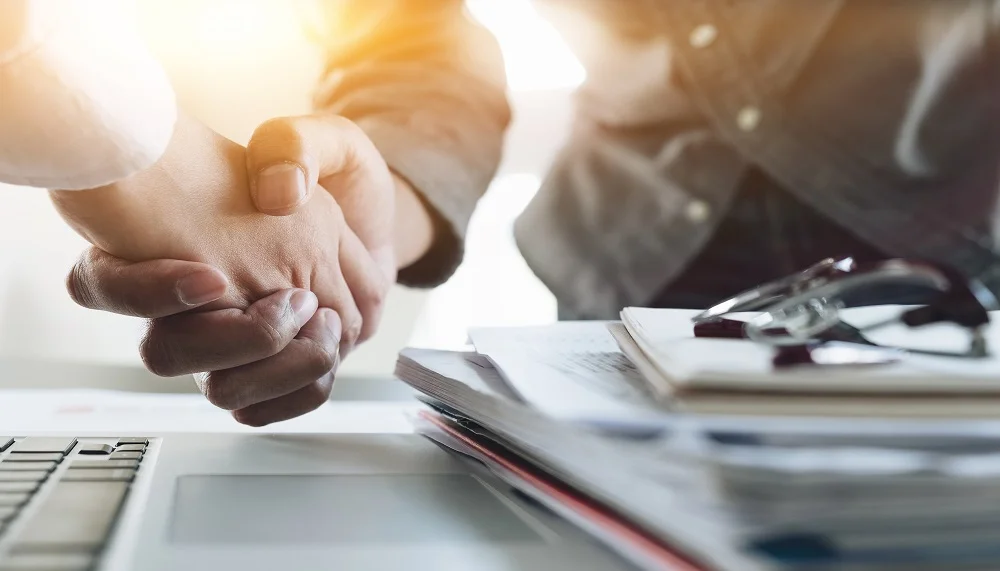 Handshake over a laptop and stacked documents