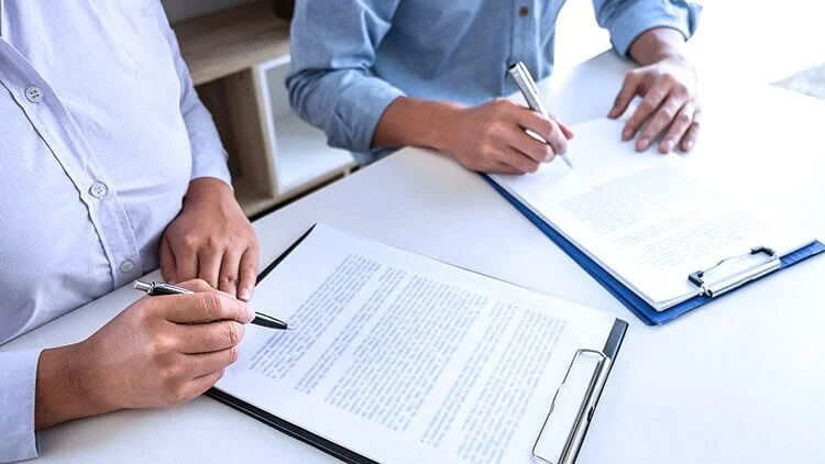 Two people signing documents on clipboards at a white desk