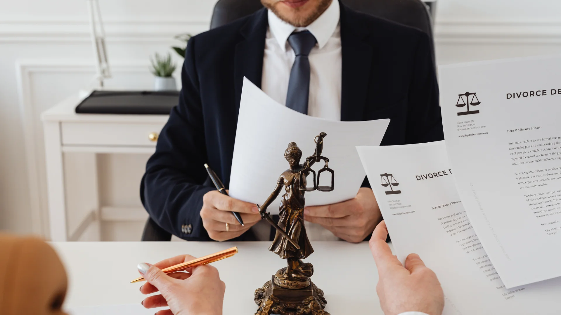 Man in a suit holding divorce papers at a desk behind a Lady Justice statuette